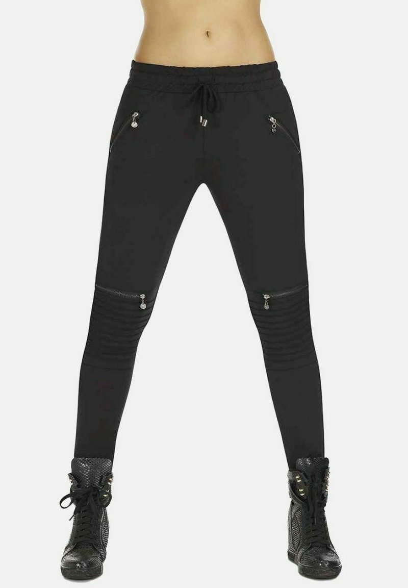 Czarne spodnie sportowe z zamkami błyskawicznymi w kieszeniach, szczegółami w żebrowanym designie oraz elastycznym pasem ze sznurkiem. W zestawie z czarnymi sneakersami za kostkę.