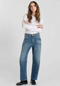 Jean en denim bleu clair avec une coupe droite, comprenant deux poches avant et des détails de couture subtils. Porté avec un haut blanc ajusté à manches longues.