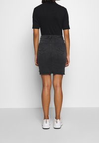 Černá džínová sukně s roztrhaným lemem, délky do poloviny stehna, se dvěma zadními kapsami a slim fit, nošená s bílými teniskami.