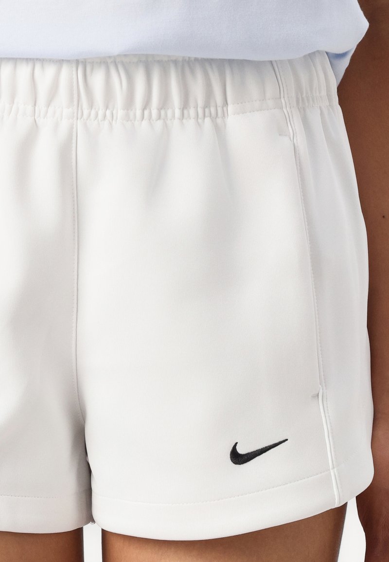 Shorts atléticos blancos con una cintura elástica y un logo de Nike negro. Presentan un material suave y ligero y un diseño sencillo.