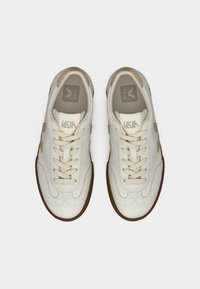 Baskets en cuir blanc avec des accents beige, bout rond, système de laçage avant, coutures ton sur ton, et semelle extérieure en caoutchouc. Logo VEJA sur la languette et le côté.