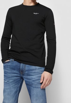 Zwart T-shirt met lange mouwen en een ronde hals, voorzien van een wit logo op de borst en geribbelde manchetten, gecombineerd met blauwe spijkerbroek.