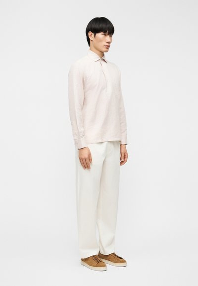 Ανοιχτό ροζ πουκάμισο με μακριά μανίκια και κουμπωτό γιακά, συνδυασμένο με άνετο λευκό παντελόνι και καφέ σουέντ παπούτσια. Απλός σχεδιασμός, άνετη γραμμή.