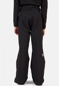 Zwarte sneeuwbroeken met een hoge taille, wijde pijpen, waterdichte stof, ritszakken en een logo nabij het onderbeen voor extra detail.