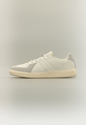 Baskets basses blanches avec accents en daim beige, fermeture à lacets et semelle en caoutchouc texturée de couleur blanc cassé, vues de profil sur un fond neutre.