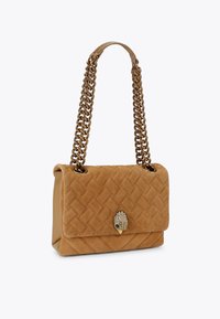 Tan suède handtas met een gequilte patroon, gouden kettinghengsels en een decoratieve sluiting met een schelpontwerp.