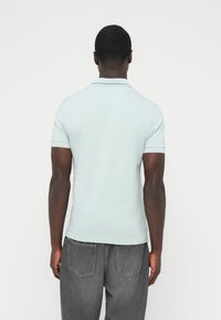 Ανοιχτό μπλε μπλουζάκι πόλο με κοντά μανίκια και γιακά, συνδυασμένο με γκρι τζιν τζιν. Το ύφασμα φαίνεται απαλό με μια διακριτική υφή.