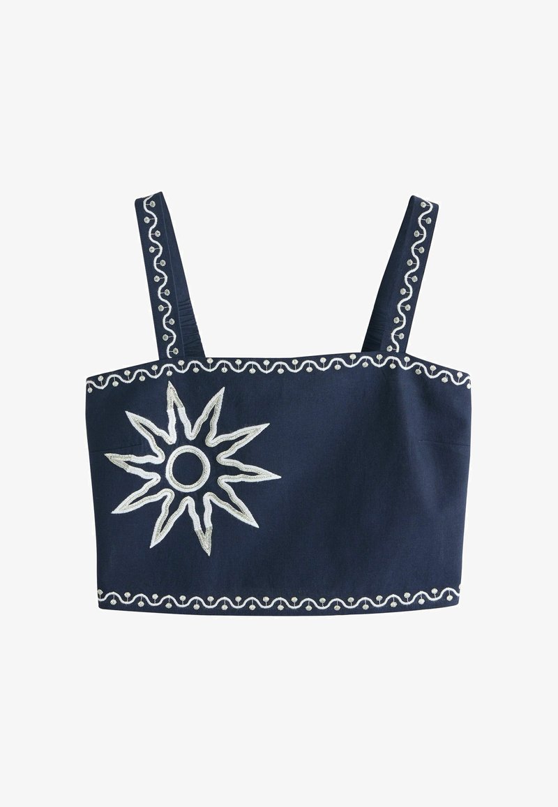 Haut court bleu marine à larges bretelles, avec un soleil brodé en blanc sur la gauche et une bordure blanche ondulée le long des bords et des bretelles.