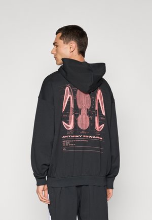 Schwarzer Kapuzenpullover mit einem großen pinken Grafikdruck auf dem Rücken, der Details des Schuhdesigns zeigt. Weicher Stoff mit lockerer Passform.