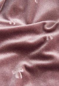 Lila Samtstoff mit weicher Textur, der dezente, geprägte Schleifen über die gesamte Oberfläche zeigt und ein zartes Muster kreiert.