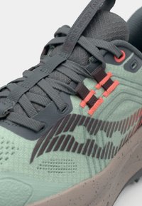 Baskets de sport vertes avec une surface texturée, des accents gris, un design rayé sur le côté et des lacets rouge vif. Semelle en caoutchouc solide.