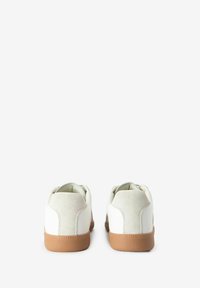 Baskets blanches avec une semelle en caoutchouc beige, présentant une finition en cuir lisse, des accents en daim au niveau du talon, et un design classique de chaussure basse.