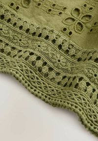 Tissu vert avec découpe florale détaillée et bordure en dentelle crochet superposée le long du bord sur un fond pâle.