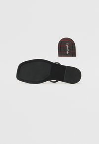 Juodi plokšti sandalai su tekstūruotu guminiu padu, su apvaliu dirželiu ir škotišku raštu iš vidinės dalies juodos ir raudonos spalvų su "Calvin Klein" logotipu.