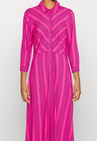 Lyserød langærmet kjole med chevronmønster i mørkeblå, knaplukning og krave, lavet af glat, letvægtsstof.