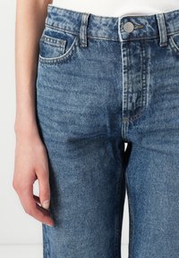 Jeans din denim de culoare bleu deschis, cu un finisaj decolorat, design cu picior drept, cinci buzunare și accesorii din metal argintiu la talie.