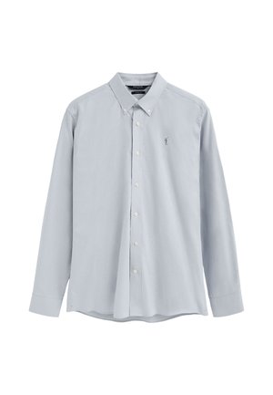 Camisa azul claro de manga larga con botones, con un pequeño logo bordado en el pecho izquierdo y un cuello abotonado.