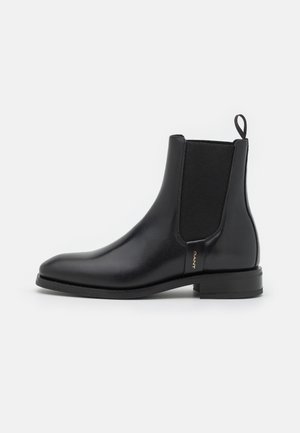 Black leather ankle boot with elastic side panel, pull tab at heel, low block heel, and a small gold logo tag on the side.