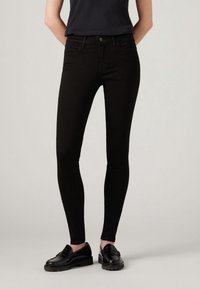 Jeans skinny de mezclilla negra con una cintura de altura media, diseño de cinco bolsillos y costuras mínimas. Combinados con mocasines negros, creando un look elegante.