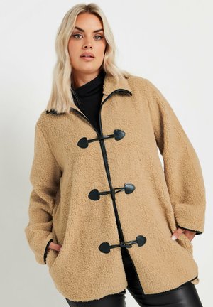 Abrigo de forro polar en color beige con cierres de piel negra, mangas largas, bolsillos laterales y un ajuste holgado. Tejido suave y texturizado en toda la prenda.