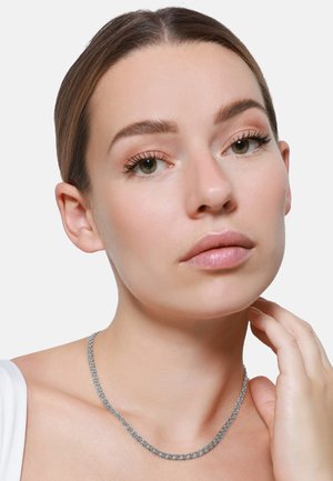 Zilveren ketting met in elkaar vergrendelde schakels, gelegen op een blote sleutelbeen. Glad metallic oppervlak dat subtiel licht weerkaatst.