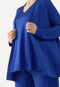 Blå lageroutfit med en långärmad öppen cardigan och en kortärmad topp, båda gjorda av mjukt tyg med V-halsdesign.