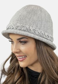 Grå strikket cloche-hat med en fletning og diskrete perle detaljer. Designet er rundt med en bred skygge, lavet af et blødt, struktureret materiale.