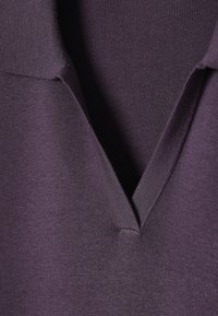 Gros plan sur un tissu tricoté de couleur violet foncé avec un col en V présentant des bords côtelés et une texture finement tissée.