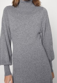 Šedý, žebrovaný rolák s dlouhými, mírně balónovými rukávy a přiléhavým střihem. Měkká textura a minimalistický design.