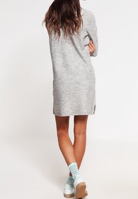 Oversized grå stickad klänning med långa ärmar, sidoclitsar och en avslappnad passform. Buren med blå rutiga strumpor och vita platåskor.