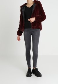 Burgundowa kurtka z sztucznego futra z kapturem, czarne wnętrze, zamek błyskawiczny, w połączeniu z szarymi obcisłymi dżinsami i czarnymi masywnymi sneakersami.