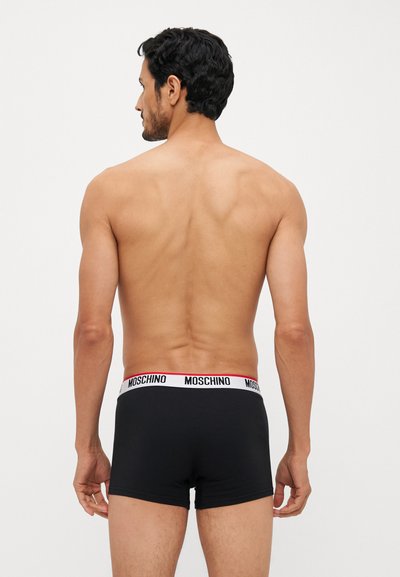 Sorte boxer shorts med en hvid og rød Moschino-logo talje. Materialet ser glat og tætsiddende ud, hvilket fremhæver et elegant design.