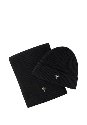 Berretto a coste nero lavorato a maglia e sciarpa abbinata, entrambi con una piccola spilla floreale d'argento su sfondo bianco.