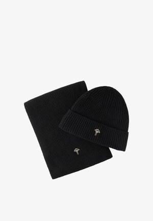 Gorro tejido de canalé negro y bufanda a juego, cada uno con un pequeño alfiler floral plateado unido sobre un fondo blanco.