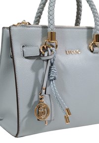 Grå håndtaske i struktureret læder med flettede håndtag, guld hardware detaljer og en aftagelig vedhæng. Har en diskret logodetalje.