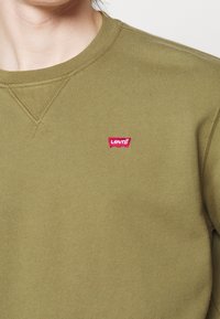 Sudadera verde oliva fabricada con tejido texturizado, que presenta un cuello redondo y una etiqueta con el logo rojo de Levi's en el pecho izquierdo.