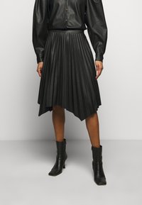 Jupe plissée noire en cuir. Elle possède une taille haute et un ourlet asymétrique, avec une texture lisse et un éclat subtil.