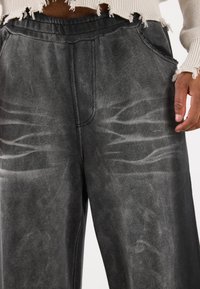 Dunkelgraue Sweatpants mit weicher Textur, die verblasste Muster und einen elastischen Bund aufweisen, ergänzt durch seitliche Taschen.