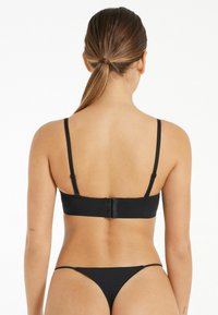 Černý bikiny top s nastavitelnými řemínky a zapínáním na háček na zádech, spárovaný s odpovídajícími černými tangy. Hladká, elastická tkanina.