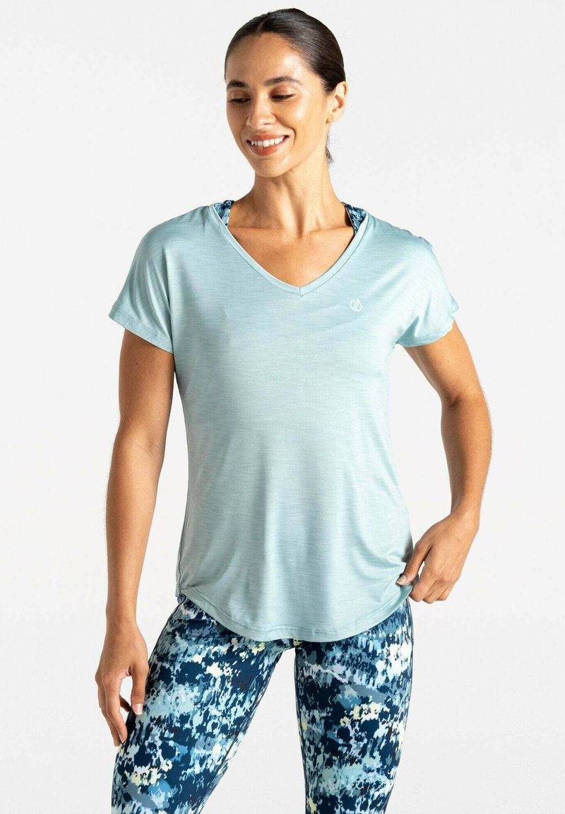 Camiseta atlética de manga corta en azul claro con escote en V, que presenta un logo sutil y un diseño drapeado sobre leggings azules con estampado.