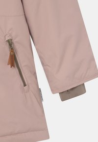 Vaaleanpunainen eristetty takki, jossa on sivuvetoketju, beige hihansuut, sileä pinta ja lappu helmoissa. Ominaisuuksiin kuuluu pyöristetty alaosa.