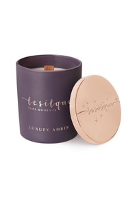 Conteneur de bougie cylindrique violet avec une mèche en bois, surmonté d'un couvercle rose gold avec du texte en relief et des étoiles, étiqueté "Amber de Luxe".