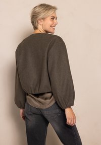Brown, cropped jacket with puffed sleeves, wool blend fabric, and a smooth, cream-colored inner shirt layered underneath, paired with dark jeans.
