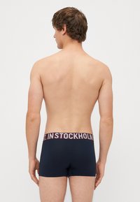 Férfi sötétkék boxer alsónadrág, bordó elasztikus derékkal, melyen fehér betűkkel az "ST. IN STOCKHOLM" felirat található. Puha, rugalmas anyagból.