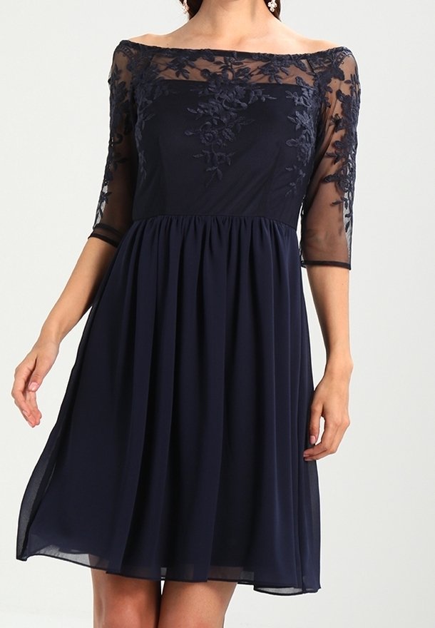 Marinblå klänning med genomskinliga trekvartsärmar, broderad blommönster på bysten, figursydd midja och flödande kjol. Texturerad tyg.