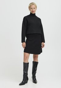 Zwarte gebreide trui met een hoge hals en ribbel manchet, gecombineerd met een zwarte mini-jurk. Glanzende zwarte kniehoogte laarzen met een spitse teen.