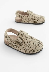 Braun gefleckte Slipper mit flacher schwarzer Sohle, einer großen Schnalle und offenem Rücken für bequemes Anziehen. Wildlederähnliche Textur.
