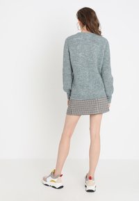 Pull en tricot bleu clair avec texture côtelée, assorti à une jupe à carreaux noir et blanc. Les chaussures présentent des accents de couleur audacieux.