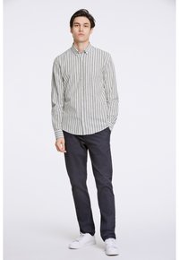 Camisa de botones con rayas verticales en gris claro y blanco. Mangas largas, cuello tipo spread, combinada con pantalones azul marino y zapatillas blancas.