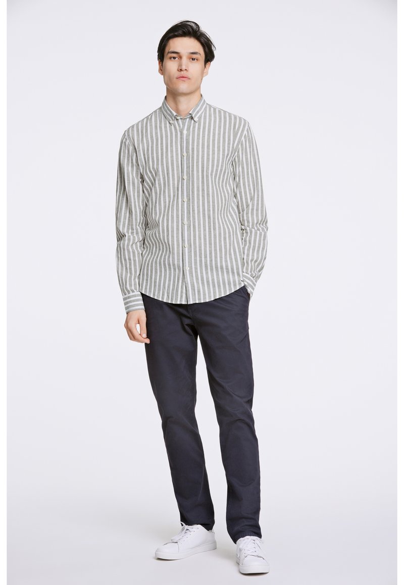 Camisa de botones con rayas verticales en gris claro y blanco. Mangas largas, cuello tipo spread, combinada con pantalones azul marino y zapatillas blancas.